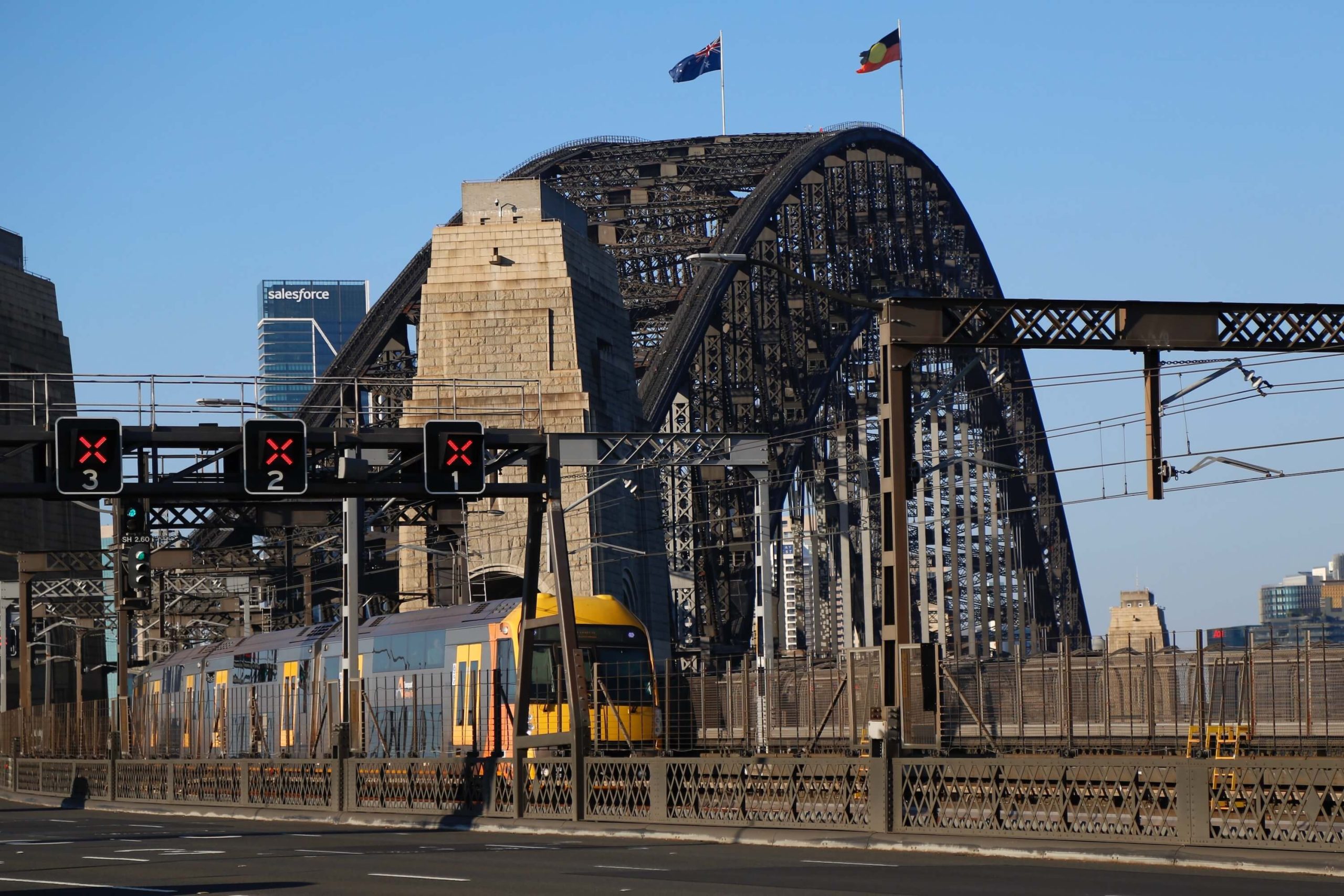 A train travels across the Sydney Harbour Bridge, viewed from the pedestrian footpath on the northern side of the bridge